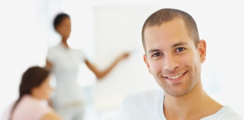 Portrait of a smiling man at work with co-workers holding a meeting in the background.